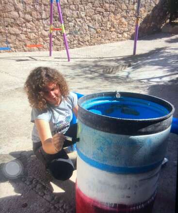The image depicts a person standing in front of a large body of water, with a small boat or raft floating on the water\'s surface. The person is wearing a hat and appears to be engaged in an outdoor activity.