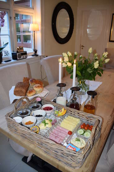 The image depicts a breakfast basket on a dining table, featuring an assortment of food items, including cheese, ham, bread, and fruit, arranged in a wicker basket.