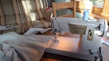 Das Bild zeigt eine Nähmaschine auf einem Tisch, mit weißem Hintergrund und ein paar verstreuten Gegenständen. Die Gesamtatmosphäre lässt auf einen gemütlichen und organisierten Raum schließen.