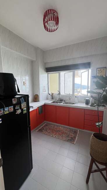 This kitchen features red cabinets, a black fridge with magnets, a patterned rug, tile walls, large windows, a potted plant, and modern countertop appliances.