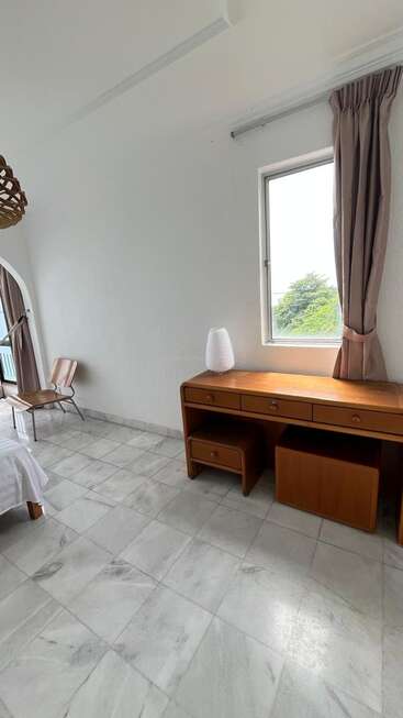 This image shows a minimalistic bedroom with a marble tile floor, wooden desk, modern lamp, window with curtains, and a simple chair in the corner.