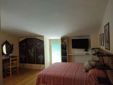 Cette chambre mansardée confortable dispose d'un lit à rayures roses, d'une armoire décorative, d'une télévision, d'étagères, d'un petit bureau avec une chaise et d'œuvres d'art encadrées qui ornent des murs aux couleurs douces.