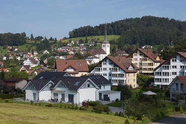 L'image représente une scène sereine d'une petite ville avec un clocher d'église, entourée d'arbres et d'un plan d'eau, évoquant un sentiment de tranquillité et de paix.