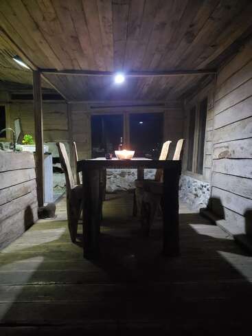 Uma área de jantar de madeira rústica com uma mesa e duas cadeiras, iluminada calorosamente por uma única lâmpada suspensa, cria uma atmosfera aconchegante e convidativa para uma refeição íntima.