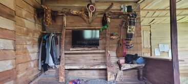 Este quarto aconchegante em cabana de madeira apresenta decoração rústica, TV, roupas penduradas, violão, livros, cobertores dobrados e prateleiras de madeira criativas feitas de galhos de árvores. Uma atmosfera calorosa e convidativa.