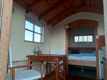 This cozy wooden cabin features a small table with two chairs, a bed with folded towels, windows for natural light, and rustic charm throughout the space.