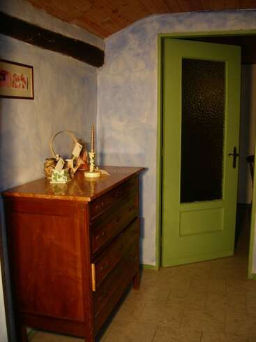 Esta acogedora habitación cuenta con paredes azules con textura, una puerta verde entreabierta, una cómoda de madera, objetos decorativos, un cuadro enmarcado y un techo inclinado de madera.