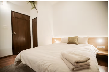 The image presents a serene bedroom scene, featuring a bed, mirror, and wooden door, with a focus on neutral tones and clean lines, evoking a sense of calm and relaxation.