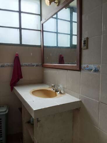 This image shows a simple bathroom with a yellow sink, large mirror, frosted windows, tiled walls, a maroon towel hanging, and a fluorescent light fixture.