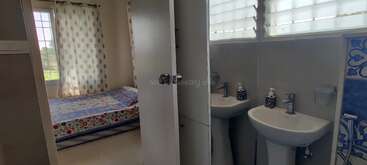 This image shows a cozy bedroom with a floral bedspread and large windows, adjacent to a bathroom with twin sinks, blue details, and mirrored walls.