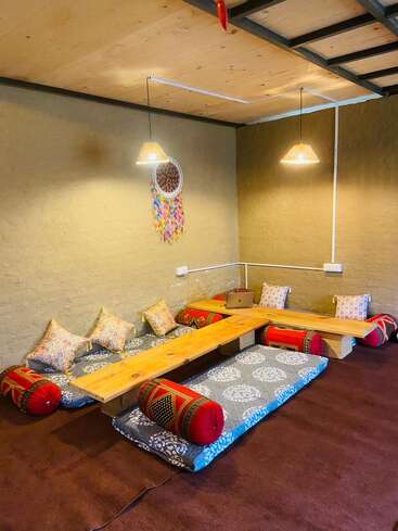 Un coin salon confortable, de style bohème, avec des tables basses en bois, des coussins de sol à motifs, des oreillers colorés, des lampes suspendues, un attrape-rêves et une atmosphère décontractée et terreuse.