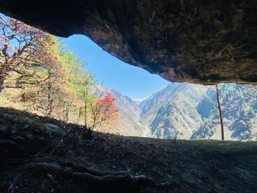 L'ouverture d'une grotte encadre un paysage de montagne vibrant, la lumière du soleil illuminant des arbres colorés, des pentes abruptes et un ciel bleu clair, créant une scène naturelle époustouflante.
