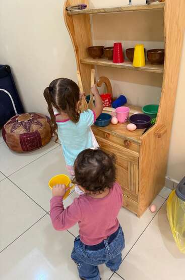Two young children play together at a wooden toy kitchen, pretending to cook with colorful cups, bowls, and utensils, learning through imaginative and interactive play.