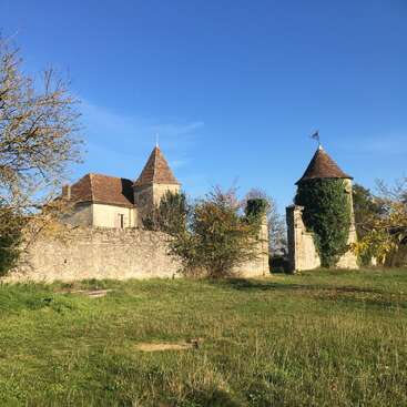 This image shows a charming, old stone building with two conical-roofed towers, surrounded by greenery and grass, under a bright blue sky. Peaceful atmosphere.