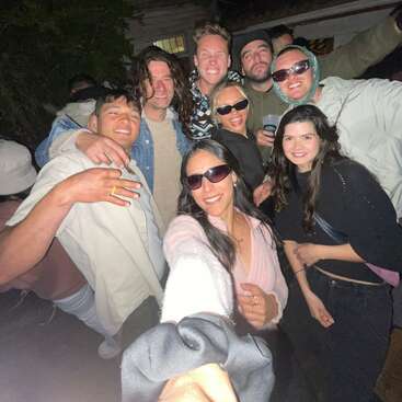 Un groupe d'amis pose de près pour un selfie de nuit. Ils sont souriants, portent des vêtements décontractés et des lunettes de soleil, et profitent d'une réunion animée en plein air.