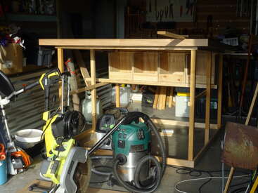 The image depicts a cluttered garage with various tools and equipment, including a workbench, power tools, and other machinery, in a dimly lit environment.