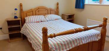 L'image représente une chambre à coucher avec un lit, une commode et une table de nuit, avec un cadre en bois et un matelas blanc, sur un fond de couleur neutre. La pièce est bien éclairée et organisée.