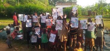 Eine Gruppe von Kindern im Freien zeigt stolz ihre bunten Zeichnungen, lächelnd und zusammen stehend, während einige auf dem Boden sitzen, umgeben von üppigem Grün und Sonnenlicht.