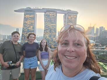 Four people pose for a cheerful photo at sunset in Singapore, with the iconic Marina Bay Sands hotel forming a stunning background against the city skyline.