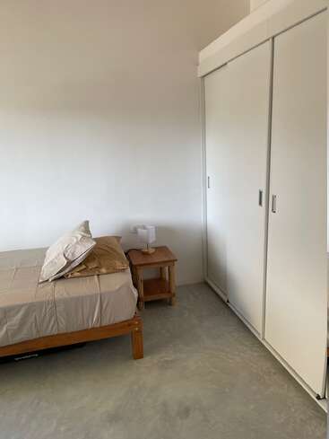 Dieses Bild zeigt ein minimalistisches Schlafzimmer mit einem Einzelbett, neutraler Bettwäsche, einem Nachttisch aus Holz, einer kleinen Lampe und einem großen weißen Schiebetürenschrank.