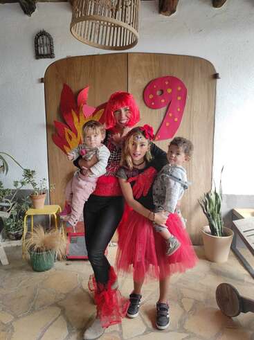 L'image représente une femme et deux enfants posant pour une photo devant une toile de fond en bois, ornée d'un grand chiffre 9 rouge et d'éléments décoratifs.