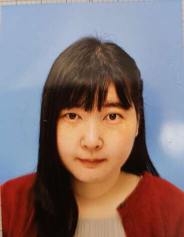 Cette image montre plusieurs copies d'une photo de type passeport représentant une femme aux cheveux raides et foncés, vêtue d'un pull rouge, sur fond bleu, disposées sur une table.