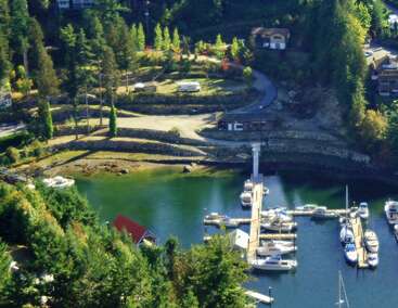 L'image représente une scène de marina sereine, avec un quai avec des bateaux, un petit bâtiment et une route menant à une maison, entourée d'arbres et d'un plan d'eau.