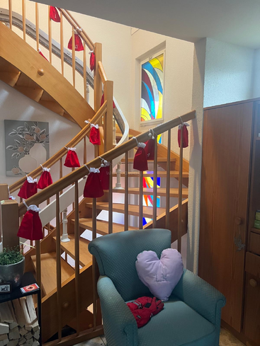 A cozy room with a spiral wooden staircase decorated with red pouches, stained glass window, green armchair with a heart-shaped pillow, and wood storage.