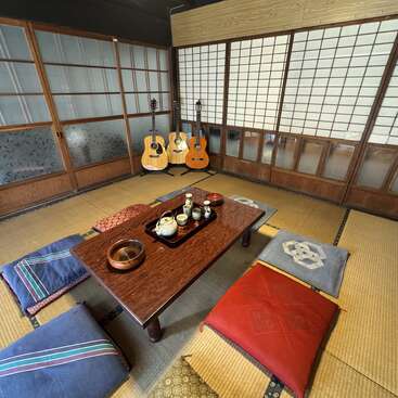 Este é um quarto tradicional japonês com tatames, uma mesa baixa de madeira, várias almofadas no chão, três violões e portas de shoji ao longo das paredes.