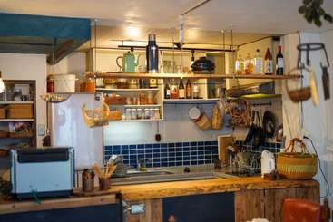 The image depicts a kitchen with a table and chairs, featuring a large window, a fireplace, and a dining area, with a table and chairs in the center of the room.