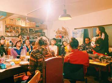 The image depicts a group of people gathered in a kitchen, surrounded by food and drinks, with a warm and inviting atmosphere.