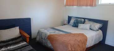 Este acogedor dormitorio cuenta con una cama de matrimonio con ropa de cama estampada, varias almohadas, una manta naranja, una cama individual, paredes claras y una pequeña ventana.