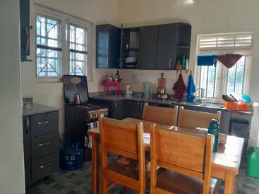 This kitchen features wooden chairs around a dining table, modern dark cabinets, a gas stove, sink area, and sunlight streaming in through two windows.