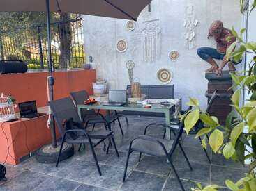 Esse pátio ao ar livre tem uma mesa com laptops, cadeiras, apanhadores de sonhos na parede, um guarda-sol grande e uma estátua do Homem-Aranha em um canto.