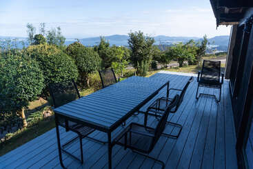 A peaceful wooden deck with a modern black table and chairs, surrounded by greenery, overlooks distant mountains and a serene blue sky. Perfect outdoor retreat.