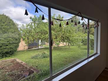 A large window overlooks a green backyard with trees, a garden bed, and a shovel. Triangle-shaped decorations hang indoors, creating a cozy and inviting scene.