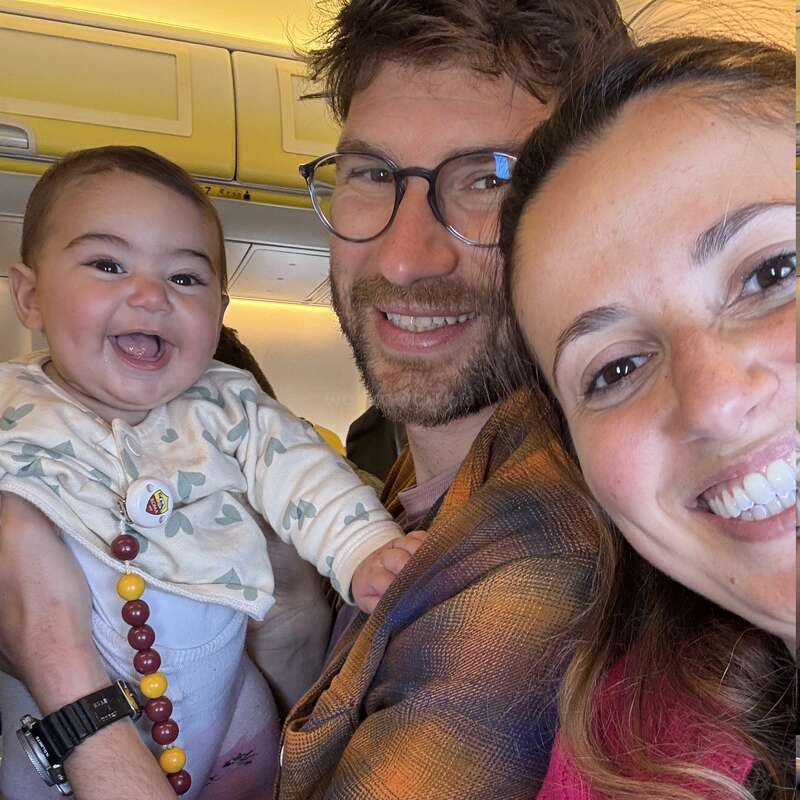 Un joyeux selfie familial dans un avion : un bébé souriant, un père à lunettes et une mère, tous trois très proches les uns des autres, rayonnant de bonheur et d'excitation à l'idée du voyage qui les attend.