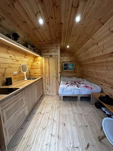 Cette cabane chaleureuse est dotée de murs, d'un plafond et d'un sol en bois, d'une cuisine compacte, d'un lit confortable, d'un éclairage tamisé, d'une petite fenêtre et d'une décoration minimaliste et rustique dans toutes les pièces.