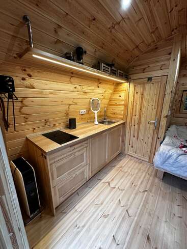 Cette photo montre une cuisine de chalet en bois, à la fois confortable et compacte, équipée d'une cuisinière, d'un évier, d'une étagère, d'un radiateur et d'un petit lit dans un coin. Un éclairage chaleureux renforce cette atmosphère douillette.