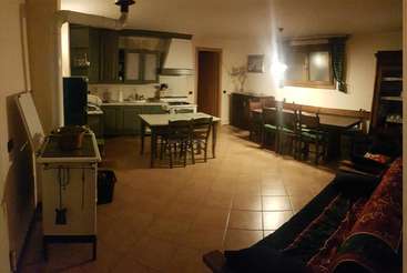 The image depicts a kitchen area with a table and chairs, featuring a large window, a sink, and a stove, with a dining table and chairs in the background.