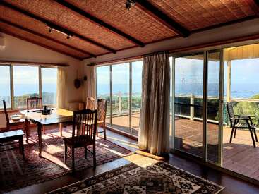 Comedor soleado con muebles de madera, acogedoras alfombras y grandes puertas acristaladas que dan a una terraza. La sala ofrece unas impresionantes vistas al mar y un ambiente tranquilo y acogedor.