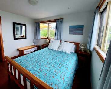 Esta acogedora habitación cuenta con una cama de madera con una colcha azul con motivos florales, almohadas blancas, grandes ventanas con cortinas ligeras, mesitas de noche y un espejo.