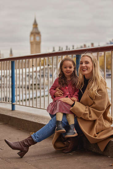 Das Bild zeigt eine Frau und ein junges Mädchen, die an einem Geländer auf dem Boden sitzen, während im Hintergrund der berühmte Uhrenturm Big Ben zu sehen ist.