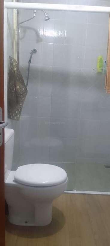 Das Bild zeigt ein kleines Badezimmer mit einer Toilette, einer Duschkabine aus Glas, zwei Duschköpfen, einem Handtuch und ein paar Pflegeprodukten auf einem Regal.
