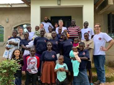 L'image représente un groupe diversifié de personnes, adultes et enfants, debout devant un bâtiment, certaines portant des chemises assorties et d'autres des vêtements décontractés.