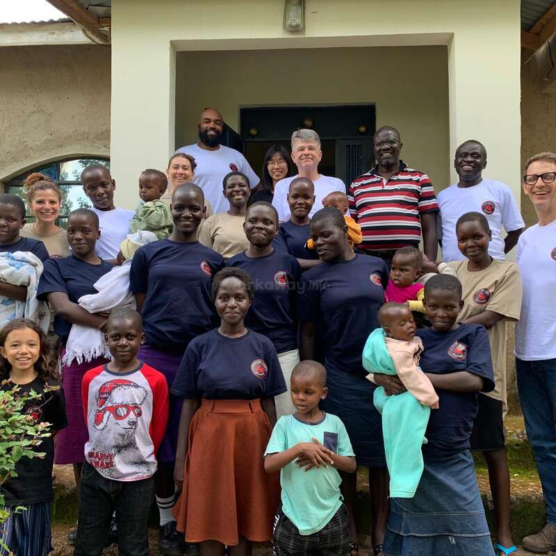 L'image représente un groupe diversifié de personnes, adultes et enfants, debout devant un bâtiment, certaines portant des chemises assorties et d'autres des vêtements décontractés.