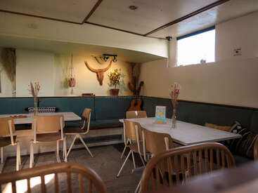 Ein gemütliches Café mit Holzstühlen, weißen Tischen und schlichter Einrichtung mit Trockenblumen, einer Gitarre, Tierschädeln und natürlichem Licht aus einem kleinen Fenster.