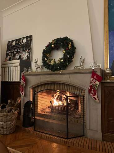 A cozy fireplace burns warmly with logs, adorned by a festive wreath, stockings, and holiday decorations, creating a welcoming Christmas atmosphere for the winter season.