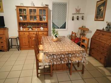 Dieses gemütliche Esszimmer verfügt über einen Holztisch mit vier Stühlen, einen Schrank, einen Schaukelstuhl, ein Fenster, dekorative Pflanzen, Kunstwerke und verschiedene rustikale, heimelige Dekorationen.