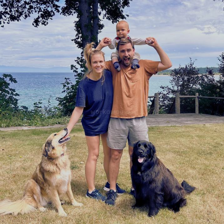 The image depicts a family of four posing for a photo, with two adults and two children, all dressed in casual attire, standing together in front of a backdrop of greenery.